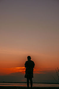 Rear view of man looking at sea against sky during sunset