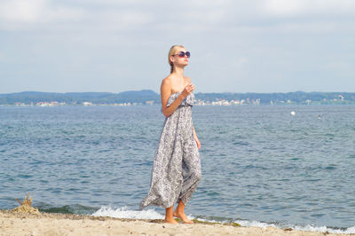 Full length of young woman standing on shore against sky