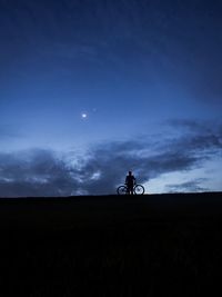 Silhouette man riding bicycle on field against sky