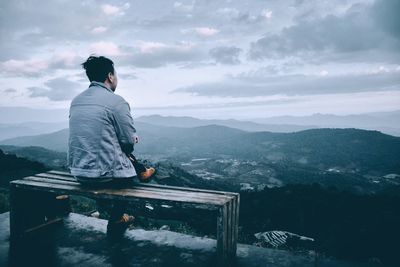 Rear view of man sitting on bench against mountain