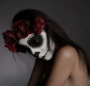 Side view of shirtless woman with spooky face paint against gray background