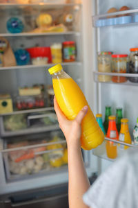 Cropped hand of woman holding juice in bottle by refrigerator