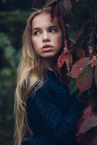 Thoughtful young woman standing by plants in forest