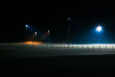 Illuminated street light on field against sky at night