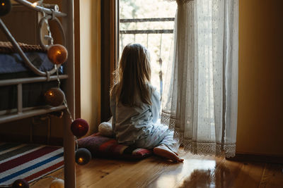 Child sitting on the floor and playing ant home. dreamy sunny mood. girl looking though the window