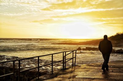 Silhouette man walking on pier by sea during sunset