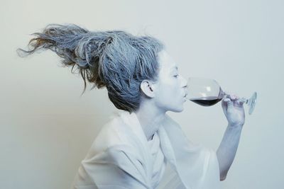 Close-up of woman drinking wine against white background