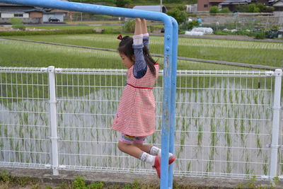 Side view of girl hanging on monkey bars against rice paddy