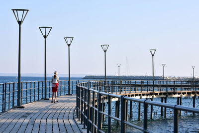 Rear view of woman standing on pier at sea against clear sky