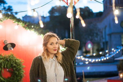 Portrait of young woman standing against house with christmas decoration at dusk