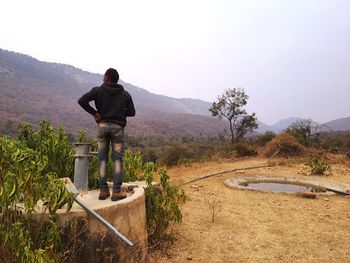 Rear view of man standing on mountain against sky