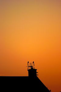Silhouette of bird on roof against orange sky
