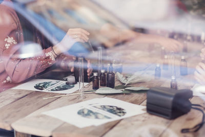 Midsection of woman mixing liquid at table in perfume workshop seen from window glass