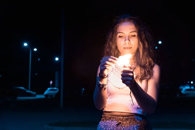 Beautiful young woman standing against illuminated lights at night