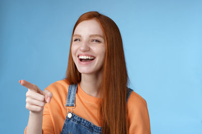 Woman laughing while pointing against blue background