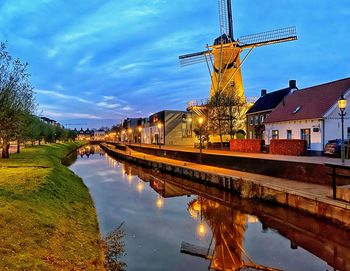 Bridge over canal amidst illuminated buildings against sky