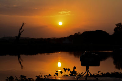 Silhouette people photographing lake against orange sky during sunset