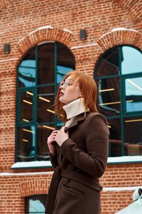 Woman looking away while standing against building