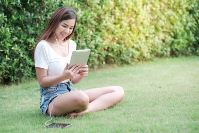 Young woman using phone while sitting on grass