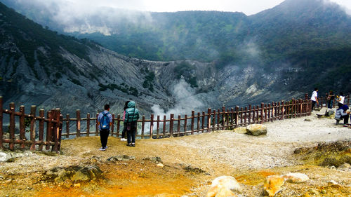 Rear view of people standing by railing on mountain