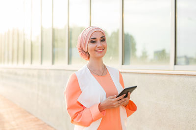 Portrait of smiling young woman standing on mobile phone