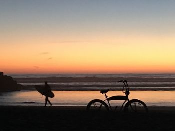 Silhouette bicycles on beach against clear sky during sunset