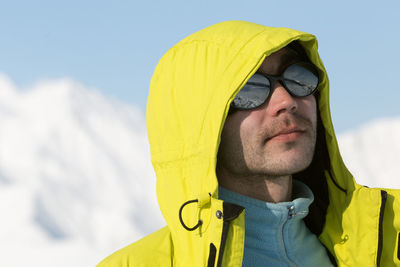 Portrait of young man in bright yellow jacket wearing mirror glasses with mountain reflection. 