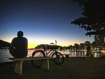 Silhouette man on bicycle by river against sky during sunset