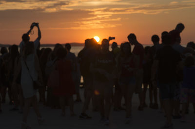 Group of people against sunset sky