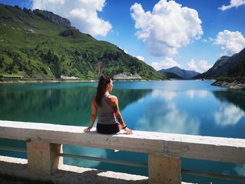 Young woman sitting on lake against sky