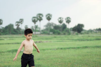 Full length of shirtless boy standing on field
