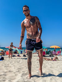 Full length of shirtless man at beach against clear blue sky