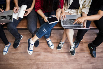 Low section of people using technologies while sitting on wooden table