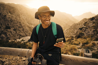 Smiling young man using smart phone while leaning on railing during vacation