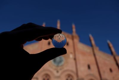 Cropped hand of person holding crystal ball against church