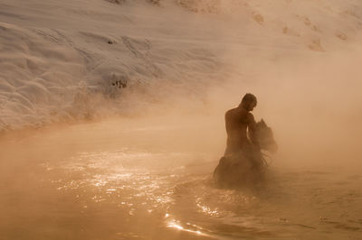 Man riding horse in muddy water during sunset