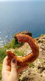 Cropped image of woman holding turkish bagel by sea