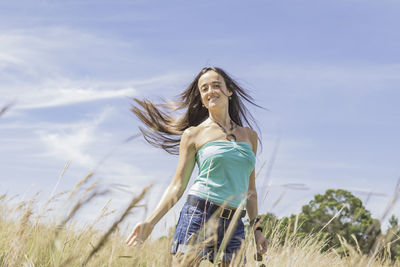 Woman flicking her hair while on field against sky. 