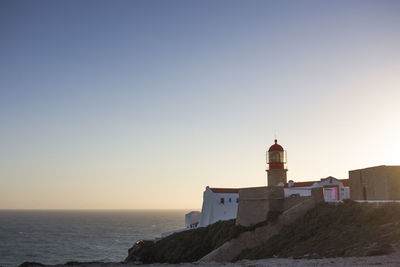 Lighthouse by sea against clear sky during sunset