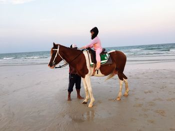 Girl riding horse at beach against clear sky