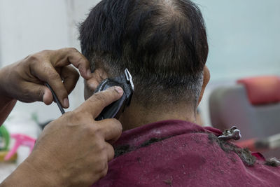 Cropped hands of barber cutting man hair in salon