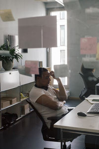 Frustrated businessman sitting on chair at office seen through glass