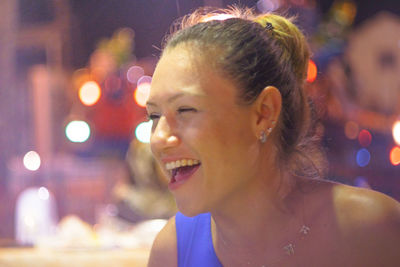 Close-up of beautiful young woman laughing against defocused lights at night