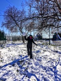 Woman throwing snowball on field against bare trees