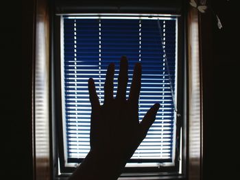 Cropped image of hand against window blinds at home