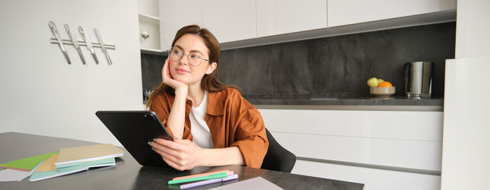 Young woman using digital tablet while sitting on table
