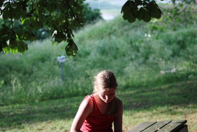 Girl sitting on bench against field at park