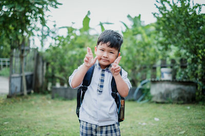 Portrait of cute schoolboy showing peace signs while standing in park
