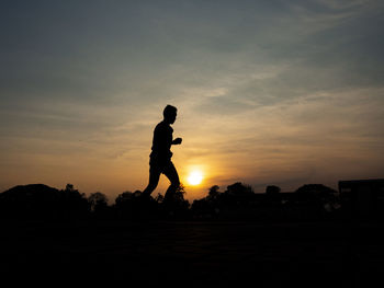 Silhouette man standing on field against sky during sunset