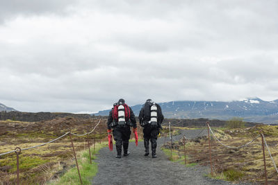 Rear view of men walking on dirt road against sky